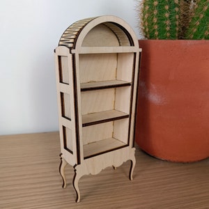 May include: A wooden display cabinet with an arched top and three shelves. The cabinet has a light wood finish and dark brown trim. It has decorative legs and is standing on a wooden surface.