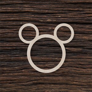 May include: White wooden cutout of a Mickey Mouse head with three circles. The cutout is on a dark brown wooden background.
