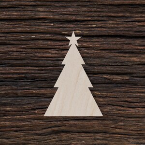 Peut inclure: Une découpe de sapin de Noël en bois blanc avec une étoile au sommet, sur un fond de bois brun foncé.