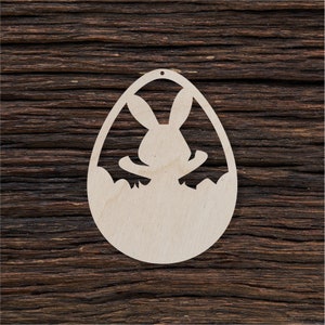 May include: A wooden Easter egg ornament featuring a cut-out design of a bunny rabbit inside. The ornament is light brown and has a hole at the top for hanging.
