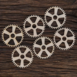 May include: Six wooden gears of different sizes arranged in a circular pattern on a dark brown wooden surface.