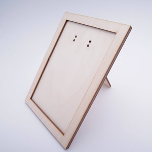 以下が含まれることがあります： 背面にスタンドが付いた明るい木製のフォトフレーム。フレームの上部に吊り下げ用の小さな穴が2つあります。