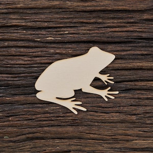 Könnte beinhalten: Eine hölzerne Silhouette einer Frosch auf einem dunkelbraunen Holzgrund.