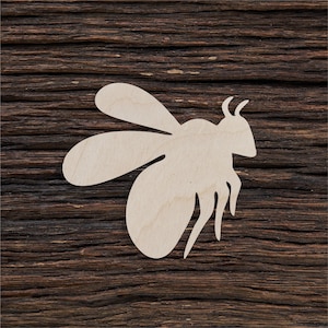 May include: A white wooden cutout of a bee on a dark brown wooden background.