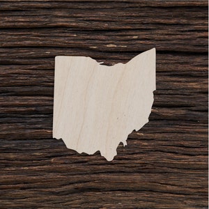 Peut inclure: Une découpe en bois de l'état de l'Ohio. La découpe est de couleur brun clair et a une surface lisse. Elle est placée sur un fond en bois brun foncé.