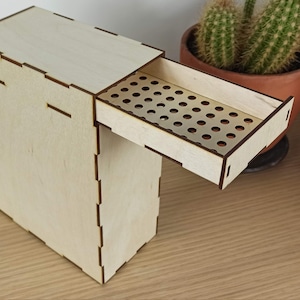May include: A wooden box with a drawer that has a perforated front. The drawer is open and the box is sitting on a wooden surface.
