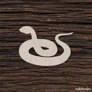 Può includere: Un ritaglio di legno color chiaro di un serpente, arrotolato in una forma circolare con la testa sollevata. Il serpente è posizionato su una superficie di legno scuro e strutturato. Il ritaglio è un design semplice e stilizzato.