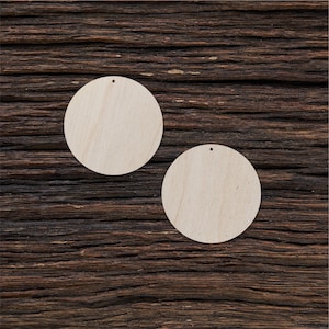 May include: Two unfinished, round wooden ornaments with a hole in the centre, on a dark brown wooden background.