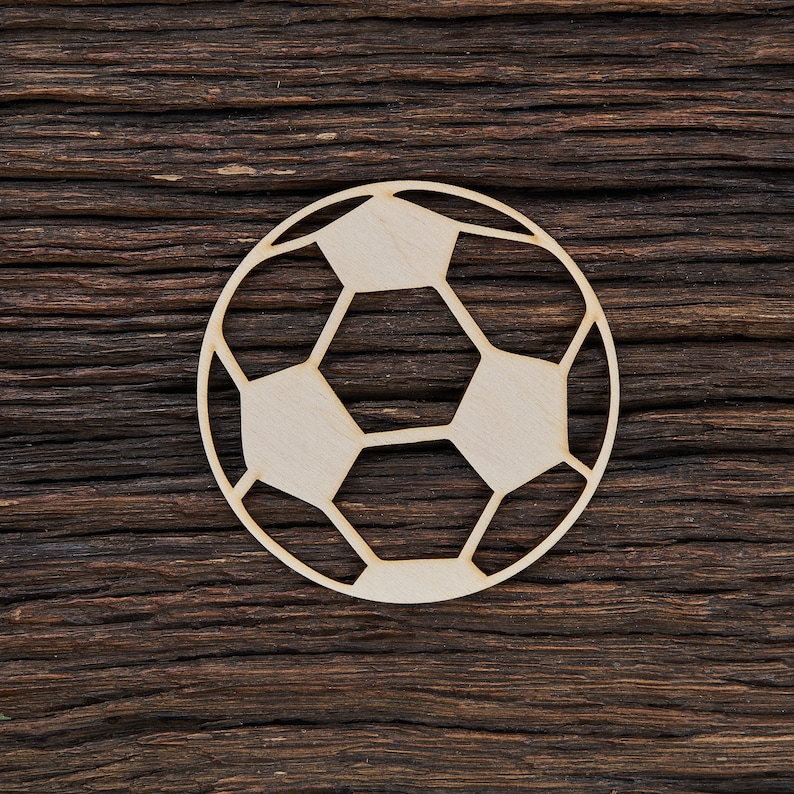 May include: A wooden cutout of a soccer ball, with a white outline on a dark brown wooden background.