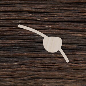 Puede incluir: Un parche de ojo de pirata de madera blanca recortado sobre un fondo de madera marrón oscuro.