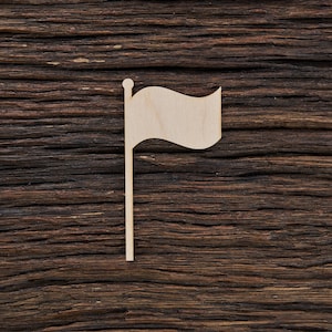 Peut inclure: Un petit drapeau en bois non fini sur un fond en bois. Le drapeau a un design ondulé et est attaché à un mince poteau. Le bois est de couleur claire naturelle et le fond est brun foncé avec un grain de bois visible.