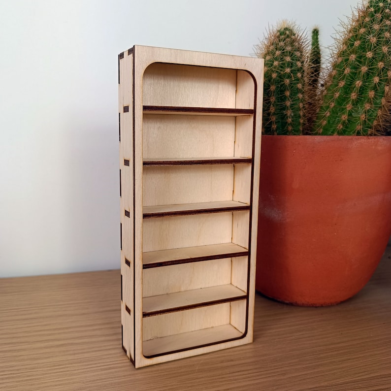 May include: A small wooden bookshelf with five shelves. The bookshelf is made of light wood with dark brown trim. It is standing on a wooden surface.