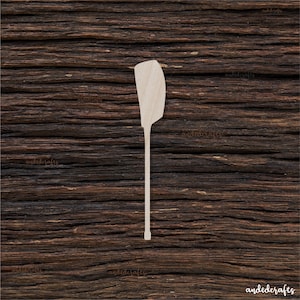 Puede incluir: Paleta de madera con forma de paleta de canoa. La paleta es de color marrón claro y tiene una pala redondeada. La paleta está sobre un fondo de madera marrón.