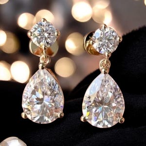 May include: A pair of gold earrings with a teardrop-shaped diamond dangling from a smaller round diamond.