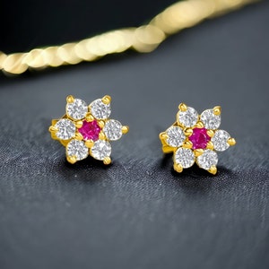 May include: A pair of gold flower-shaped earrings with a red centre stone and clear stones around it.