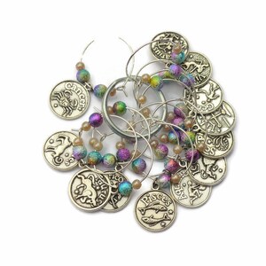 May include: Set of 12 silver-toned wine glass charms with zodiac symbols and iridescent beads. The charms feature the astrological signs: Aries, Taurus, Gemini, Cancer, Leo, Virgo, Libra, Scorpio, Sagittarius, Capricorn, Aquarius, and Pisces.