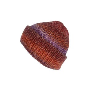May include: A knitted beanie hat featuring a variegated colour pattern of deep rust, burnt orange, and subtle streaks of violet purple. The hat is constructed with a thick, textured yarn and includes a wide, folded cuff at the bottom edge.