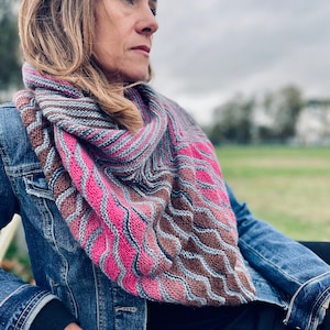 Könnte beinhalten: Eine Frau trägt eine Jeansjacke und einen gestrickten Schal in Rosa, Braun und Grau. Der Schal hat ein wellenförmiges Muster.