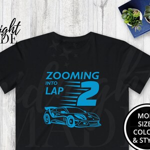 May include: Black t-shirt with a blue car graphic and the text "Zooming into Lap 2." The shirt also has a circular graphic that says "More Sizes, Colors, & Styles."