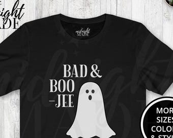 May include: Black t-shirt with the text "BAD & BOO -JEE" and a white ghost graphic. The shirt is displayed with blue jeans and black sneakers, suggesting a casual, Halloween-themed style.