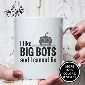 May include: White ceramic coffee mug with a black robot graphic and the text "I like BIG BOTS and I cannot lie". The mug is being held by a person's hands. The text "MORE SIZES, COLORS, & STYLES" is visible in a black circle on the bottom right corner of the mug.