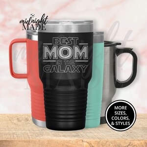 May include: Black stainless steel tumbler with a white inscription that reads "Best Mom in the Galaxy". The tumbler is next to a red and a turquoise tumbler.