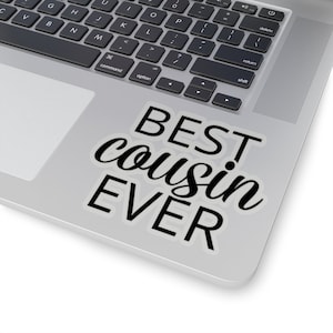 May include: A white sticker with the text "BEST cousin EVER" in a black, cursive font. The sticker is on a silver laptop, with the keyboard visible. The laptop is on a white surface.