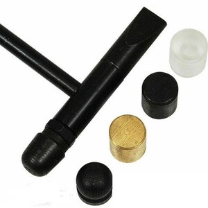 May include: A black metal tool with a T-shaped handle and a flat, angled head. Several small cylindrical pieces in black, gold, and clear plastic are arranged nearby. The tool appears to be for a specific mechanical purpose.