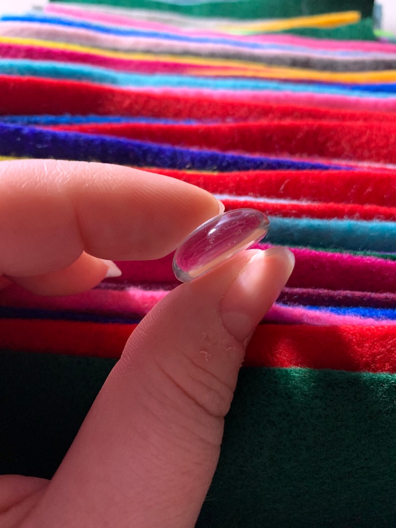 May include: A clear glass bead, held between two fingers, against a colorful striped background.
