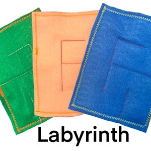 May include: Three felt squares with different colored felt and stitched lines forming a maze pattern. The squares are green, orange, and blue. The text "Labyrinth" is printed below the squares.