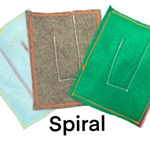 May include: Three felt squares with different colored borders and a white stitched U shape in the center. The squares are light blue, brown, and green. The text "Spiral" is printed below the squares.