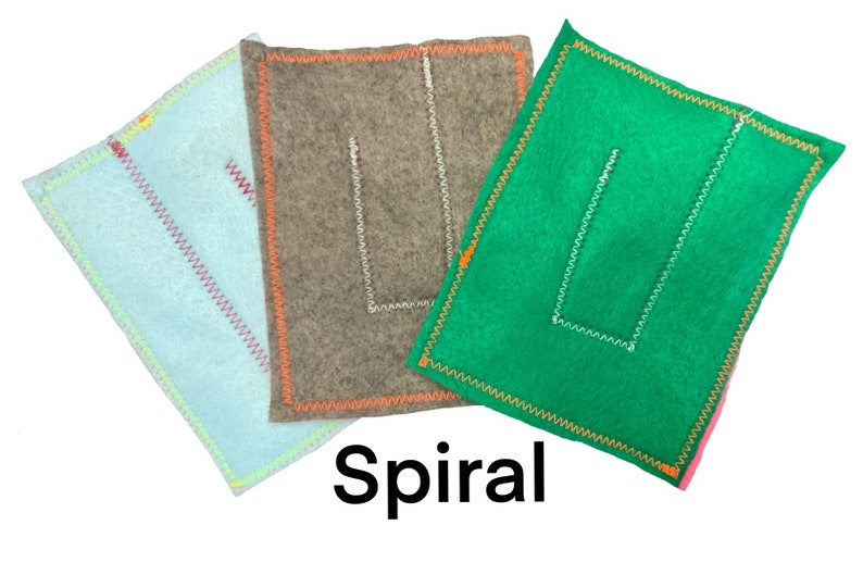 May include: Three felt squares with different colored borders and a white stitched U shape in the center. The squares are light blue, brown, and green. The text "Spiral" is printed below the squares.