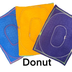 May include: Three felt squares with a donut shape cut out. The squares are blue, orange, and purple. The donut shapes are outlined in pink, yellow, and white thread.