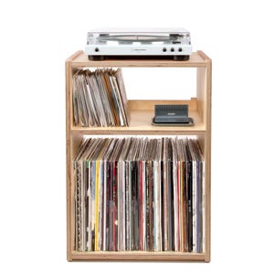 May include: A light wood record player stand with two shelves. The top shelf has a white record player on it. The bottom shelf is filled with vinyl records.