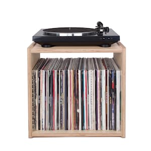 May include: A wooden record player stand with a turntable on top and shelves for storing vinyl records. The stand is made of light wood and has a simple, modern design.