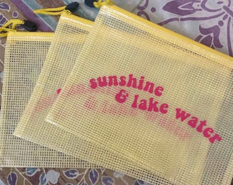May include: Three yellow mesh zippered pouches with a pink and white graphic that says "sunshine & lake water".