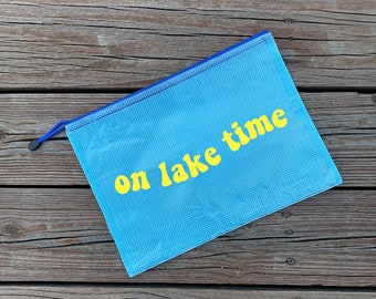 May include: A light blue mesh zippered pouch with a yellow inscription that reads "on lake time".