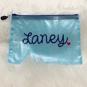 Puede incluir: Una bolsa de malla azul claro con cremallera azul marino y el nombre "Laney" bordado en azul marino con un coraz&oacute;n rojo.