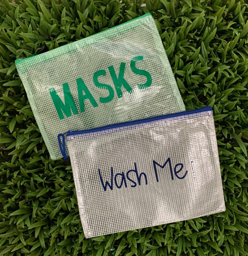 Puede incluir: Dos bolsas de pl&aacute;stico transparente con cremallera y tejido de malla. Una bolsa es verde y dice "MASKS" en letras verdes. La otra bolsa es blanca y dice "Wash Me" en letras azules.