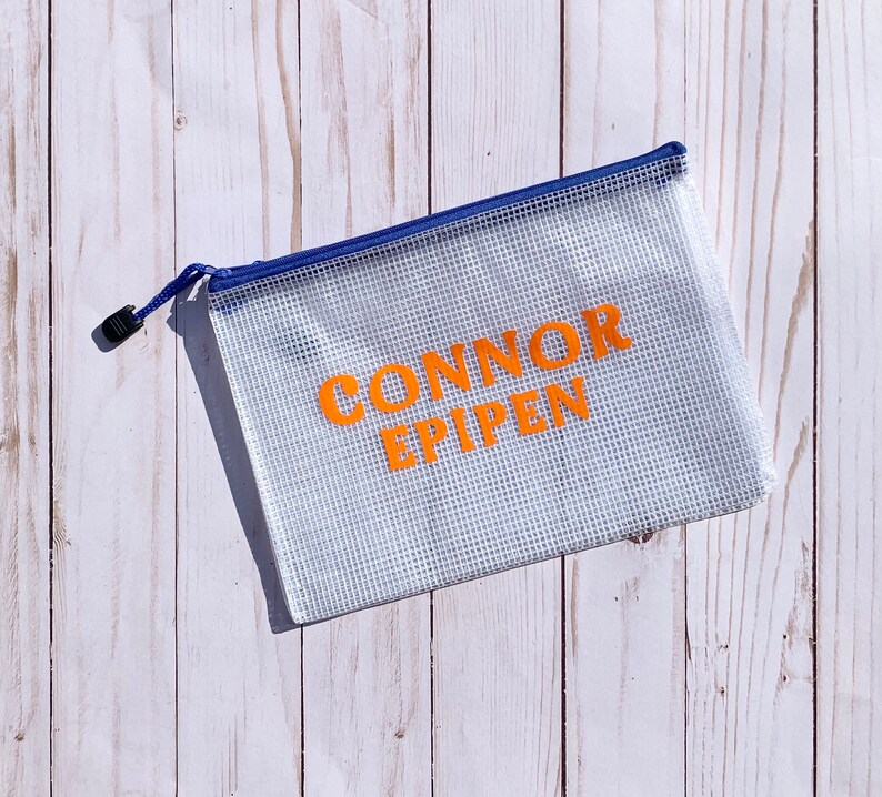 Puede incluir: Una bolsa de malla blanca con cremallera azul. La bolsa tiene las palabras "CONNOR EPIPEN" impresas en naranja.