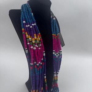 May include: A multi-strand necklace on a black mannequin. The necklace has rows of colourful beads in blue, purple, pink, yellow, green, and white. The beads are arranged in a pattern, creating a vibrant and eye-catching accessory.