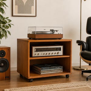 May include: A wooden media console on casters featuring an open shelf design. The top surface holds a turntable with a clear dust cover. The middle shelf contains a silver-faced stereo receiver, and the bottom shelf holds a stack of vinyl records.