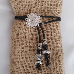 May include: A black elastic hair tie with a silver filigree charm and black and clear beads.