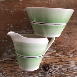 Peut inclure: Un ensemble de deux pièces de vaisselle en céramique verte et blanche. Un pichet crème avec un motif vert dégradé et une bande noire autour du milieu. Un bol vert et blanc avec une bande noire autour du milieu.