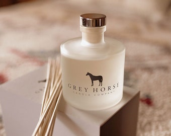 May include: A white frosted glass diffuser bottle with a silver cap, resting on a white box. The bottle has the text "GREY HORSE CANDLE COMPANY" and a horse silhouette. A bundle of wooden reeds sits beside the bottle.