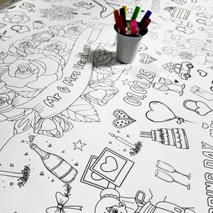 Könnte beinhalten: Ein weißes Ausmalblatt zum Thema Hochzeit mit verschiedenen Illustrationen, darunter Rosen, Champagner, eine Torte und ein Auto mit dem Text "JUST MARRIED". Das Blatt zeigt auch das Datum "01.08.25" und die Namen "Mr & Mrs Henshaw". Ein kleiner silberner Becher mit bunten Markern befindet sich im Bild.