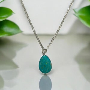 Puede incluir: Un collar de cadena de plata con un colgante de turquesa en forma de lágrima.