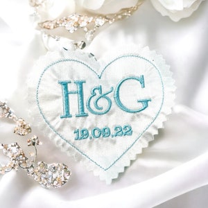 Peut inclure: Un patch en tissu blanc en forme de cœur avec une broderie bleue. Le patch dit "H&G" et "19.09.22".