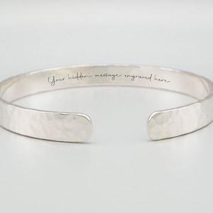 May include: A silver hammered bangle bracelet with a hidden message engraved on the inside. The message reads "Your hidden message engraved here".