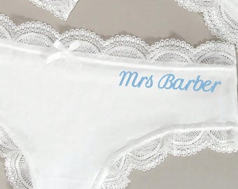 May include: White underwear with delicate lace trim and a small bow. The text "Mrs Barber" is embroidered in light blue. Several pieces are visible, suggesting a set.